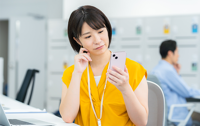 スマートフォンを見て悩む女性のイメージ